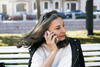 an older woman talking on a cell phone outdoors on a bench